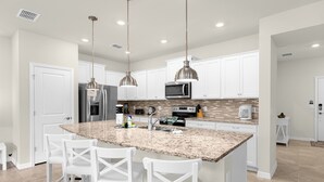 Una cocina moderna con armarios blancos, encimeras de granito, electrodomésticos de acero inoxidable e iluminación colgante.