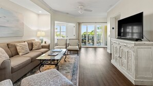 Amplia sala de estar con un sofá color beige, una mesa de centro y un televisor sobre un mueble blanco.