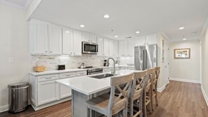 Una cocina moderna con armarios blancos, electrodomésticos de acero inoxidable y una isla central con taburetes de bar.