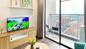 A modern living room with a flat-screen TV, a wooden entertainment unit, a vase with flowers, and a balcony with a city view. - It Dust Homestay 6 - the Forest Apartment (Hanoi)