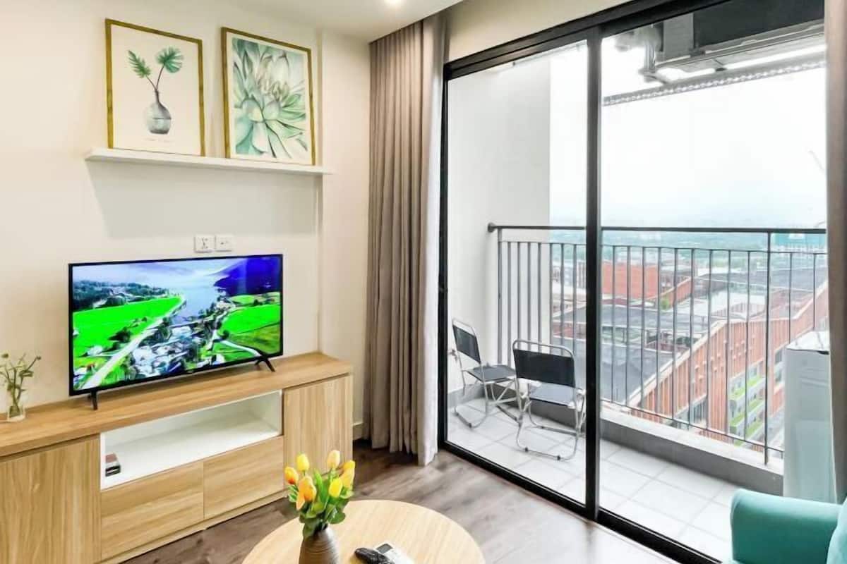 A modern living room with a flat-screen TV, a wooden entertainment unit, a vase with flowers, and a balcony with a city view.