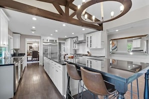 A modern kitchen with a central island, stainless steel appliances, and a chandelier.