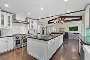 A modern kitchen with white cabinetry, a large island, stainless steel appliances, and a wooden floor.