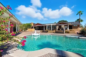 Une piscine avec un cygne gonflable blanc, un patio couvert et une maison à l’extérieur en briques.