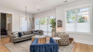 A spacious living room with a sofa, coffee table, ottoman, and large windows.