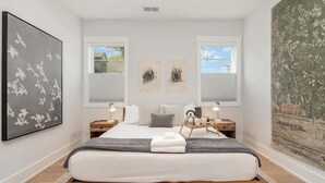 A bedroom with a bed, two bedside tables, a nightstand, a window, and artwork on the walls.