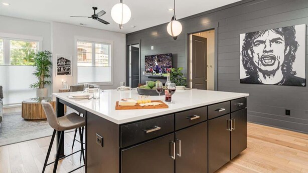 A modern kitchen with a central island, pendant lighting, and a large black-and-white artwork on the wall.