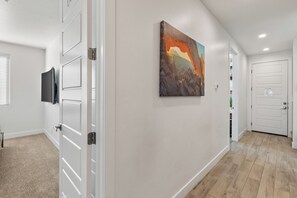 Un couloir avec un tableau, des portes blanches et un téléviseur fixé au mur.