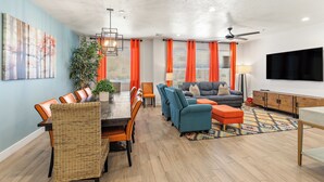 Un salon moderne comprenant un coin repas, un ensemble de canapés, un téléviseur et un ventilateur de plafond.