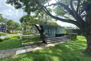 A modern building with a glass facade, a covered outdoor seating area, and a paved walkway. - Shipping Container Hotel at One-North (Singapore)