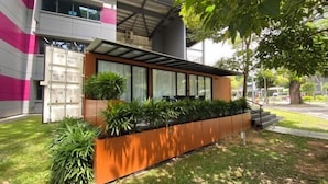 Un edificio moderno con un área de estar al aire libre cubierta, rodeado de vegetación y una escalera que conduce a un nivel superior.