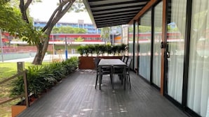 Un espacio al aire libre techado con mesa y sillas, rodeado de plantas en macetas y una terraza de madera.