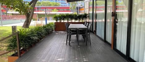 A covered outdoor seating area with a table and chairs, surrounded by potted plants and a wooden deck.