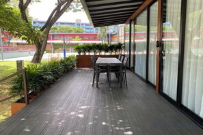 An outdoor patio with a table and chairs, surrounded by plants and a view of a sports field. - Shipping Container Hotel at One-North (Singapore)