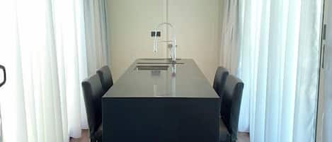Un salón de conferencias con una mesa larga, cuatro sillas, un lavamanos y cortinas blancas.