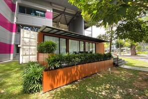 A modern building with a covered outdoor seating area and a planter with plants. - Shipping Container Hotel at One-North (Singapore)