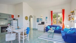 A spacious living area with a blue sofa, a dining table, and a kitchen area. - Villa Didi – Scopello, Castellamare del Golfo area (Scopello)