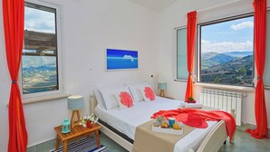 A bedroom with a bed, a window with a view of the countryside, a small table with a lamp, and a radiator. - Villa Didi – Scopello, Castellamare del Golfo area (Scopello)