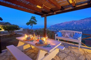 Ein Essbereich im Freien mit einem Tisch für zwei Personen, einer Bank und Blick auf eine Stadtlandschaft im Abenddämmerung.