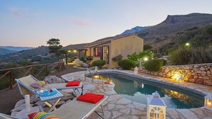 A pool area with lounge chairs and a stone deck, surrounded by a stone wall and a mountain view. - Villa Didi – Scopello, Castellamare del Golfo area (Scopello)