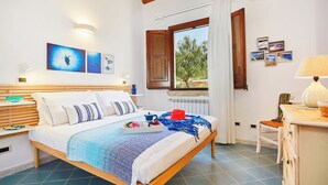 A bedroom with a bed, bedside table, lamp, and a window with curtains. - Brezza del Vento, Scopello area, Sicily (Scopello)