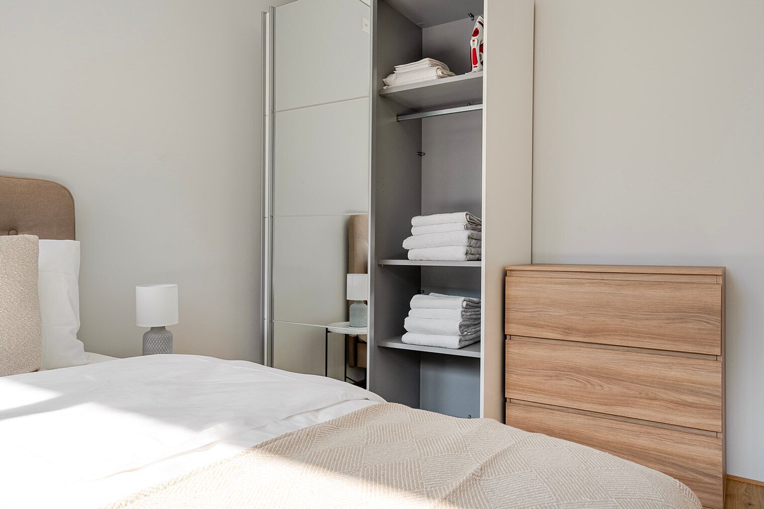 A modern bedroom with a bed, a wardrobe, and a shelf with folded towels.