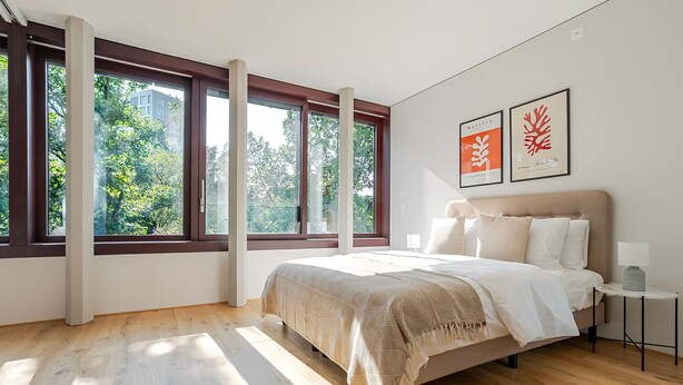 A modern bedroom with a large bed, a nightstand, and a window with a view of trees. - Blueground | Basel-Vorstaedte, view, nr Kunstmuseum (Basel)