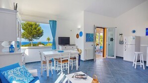 A modern living room with a dining area, a TV, and a view of the sea.
