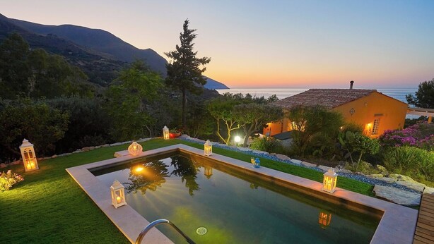 A rectangular pool with a surrounding deck, surrounded by well-maintained landscaping and a mountain backdrop.