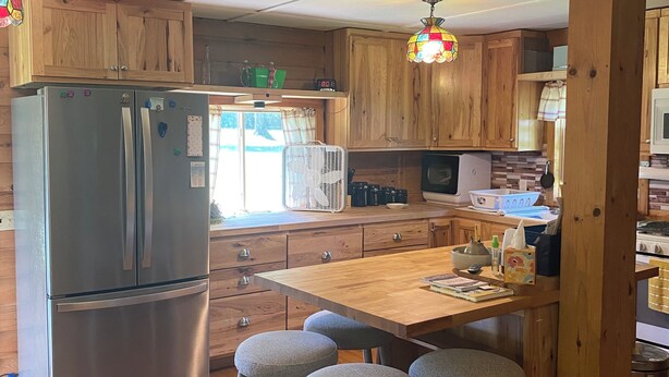 Une cuisine dotée de meubles en bois, d’un réfrigérateur en acier inoxydable, d’une table à manger en bois avec des tabourets de bar et d’un four à micro-ondes.