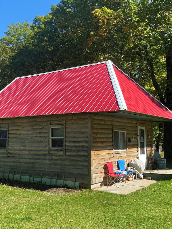 Une cabane en bois avec un toit en métal rouge, une véranda avec une chaise bleue et une petite table.