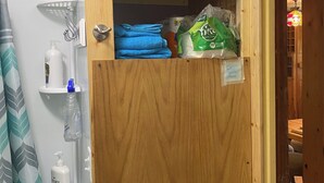 Un meuble en bois surmonté d’un récipient transparent en plastique, contenant des serviettes bleues pliées et un sac vert de lessive.