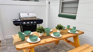 Une table en bois, dressée avec des bols et des assiettes de couleur turquoise, un gril et des plantes en pot.