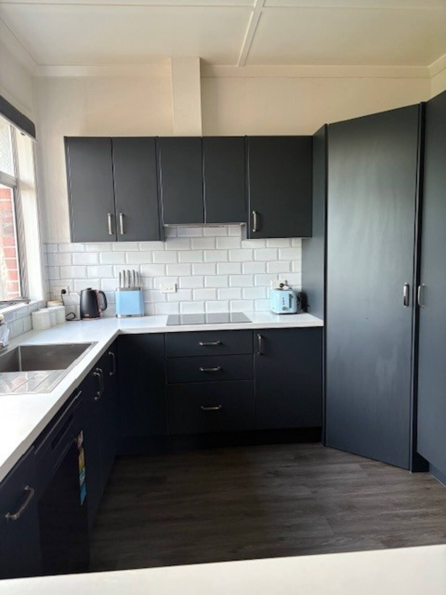 Una cocina compacta con armarios oscuros, azulejos tipo metro blancos y una pequeña encimera.