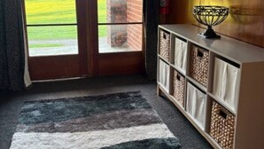 A room with a large sliding glass door leading to a brick wall, a wooden cabinet with storage bins, and a patterned rug on the floor. - Beach Valley Air B & B (Tuatapere)