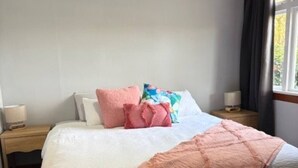 A neatly made bed with a white duvet and pink throw, accompanied by a floral pillow and a pink blanket. - Beach Valley Air B & B (Tuatapere)