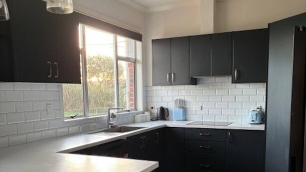 A modern kitchen with dark cabinets, a large island, and a window providing natural light. - Beach Valley Air B & B (Tuatapere)