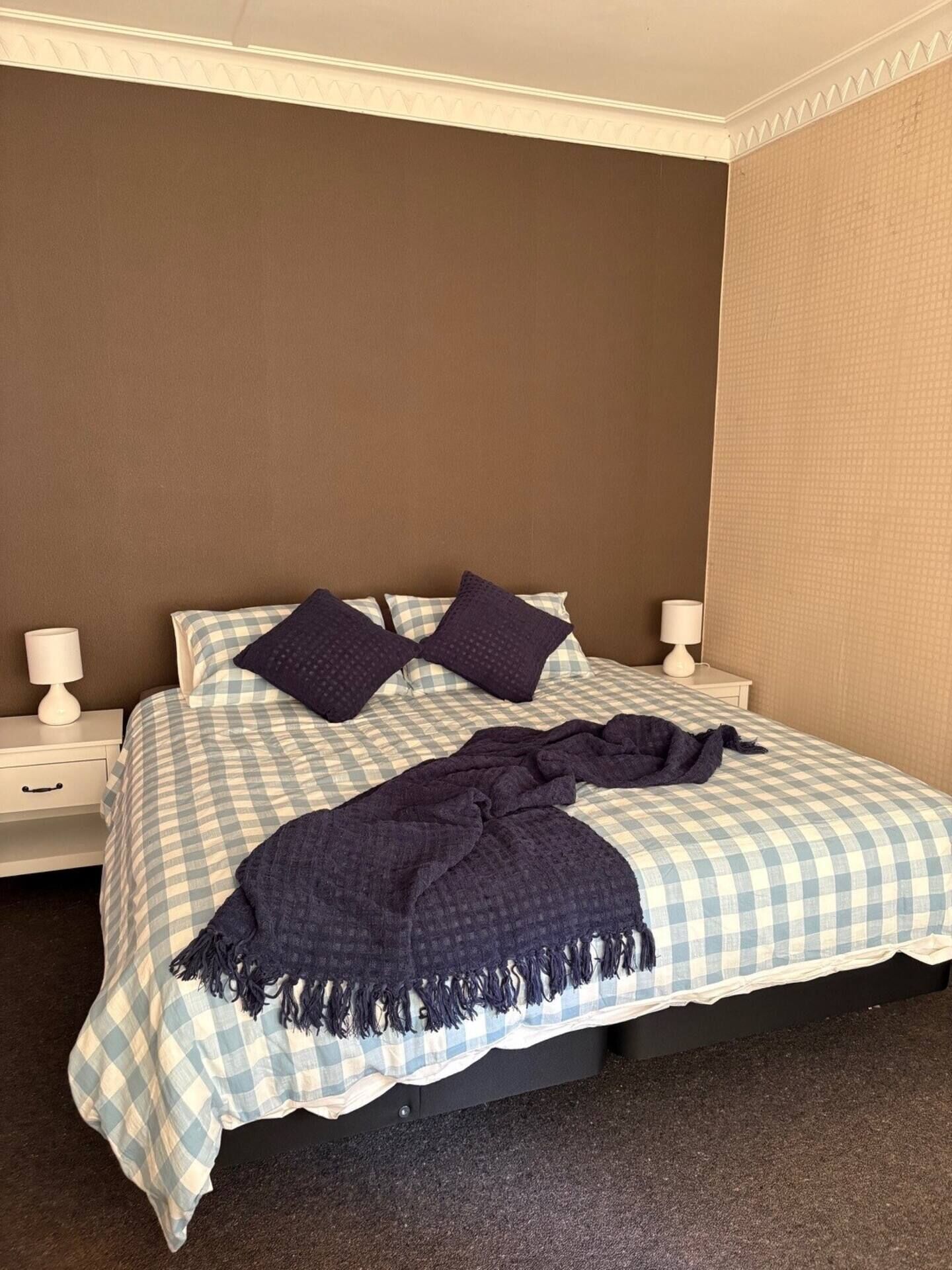 A neatly made bed with a checkered bedspread and two pillows, a dark throw blanket, and two bedside lamps on white nightstands.