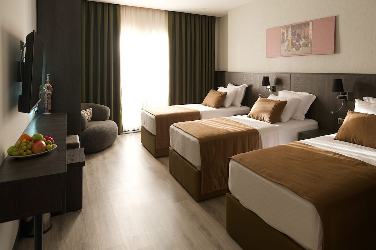 A hotel room with two beds, a desk with a fruit bowl, a TV, and a painting on the wall.