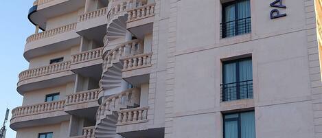 A multi-story building with a spiral staircase and balconies. The building has a sign that reads "PARK DEDEMAN".