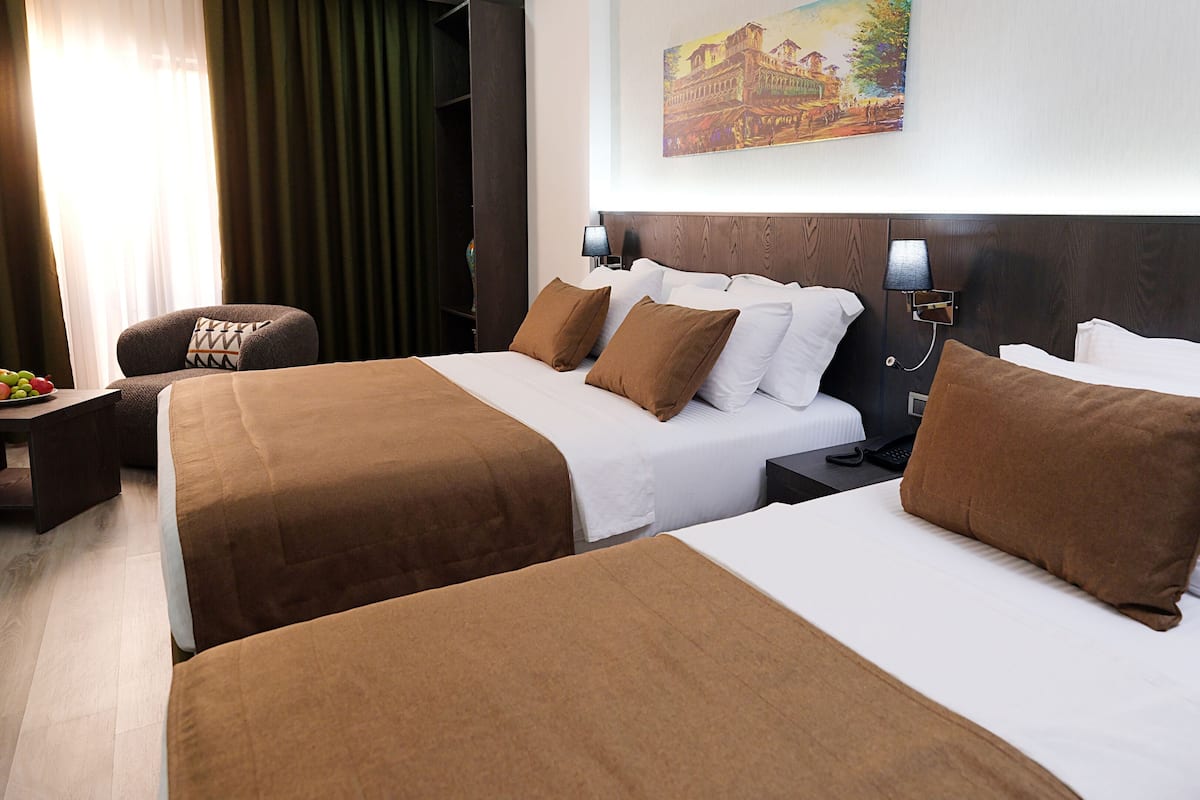 A hotel room with two beds, a desk, a chair, and a painting on the wall.