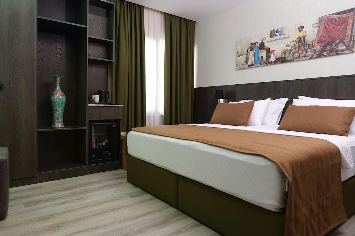 A hotel room with a bed, a desk with a vase, and a shelf with a colorful vase.
