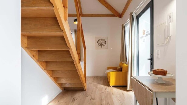 A wooden staircase leading to a living area with a yellow sofa and a table with a loaf of bread.