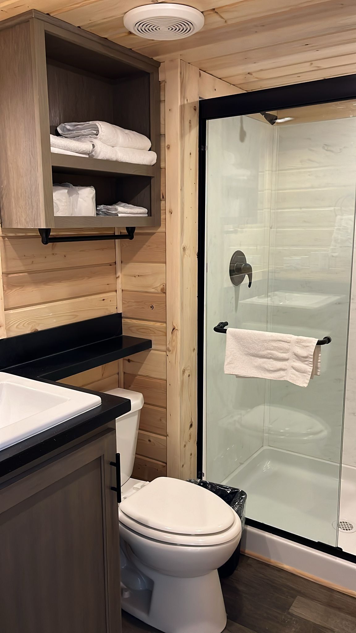 Ein Badezimmer einer Holzhütte mit Toilette, Waschbecken und Duschkabine.