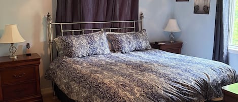 A bedroom with a bed, two bedside tables, a nightstand, a lamp, a ceiling light, and a window with curtains.