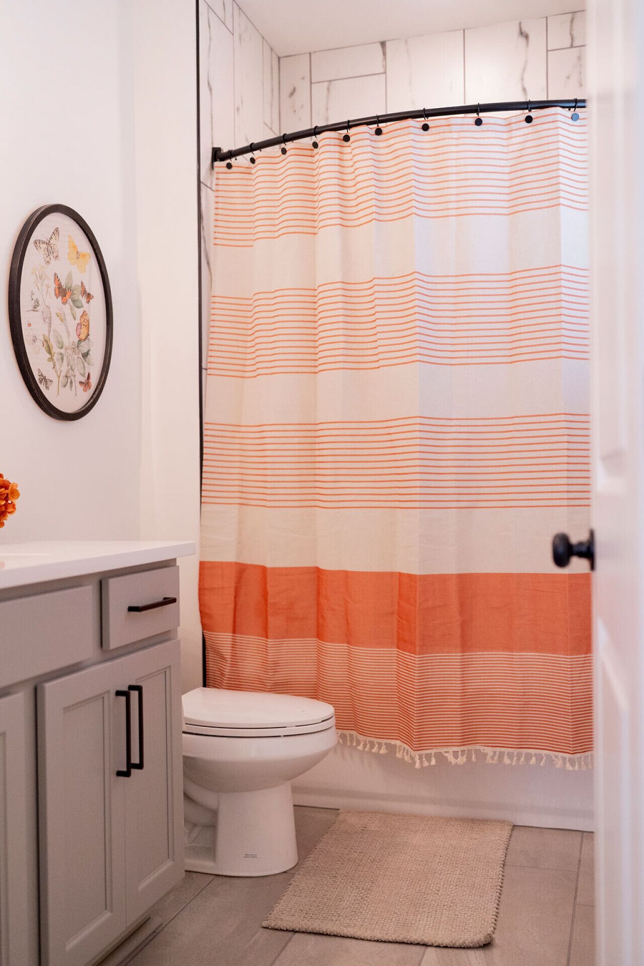 A bathroom with a striped shower curtain, a toilet, a sink with a mirror, and a framed botanical print on the wall.