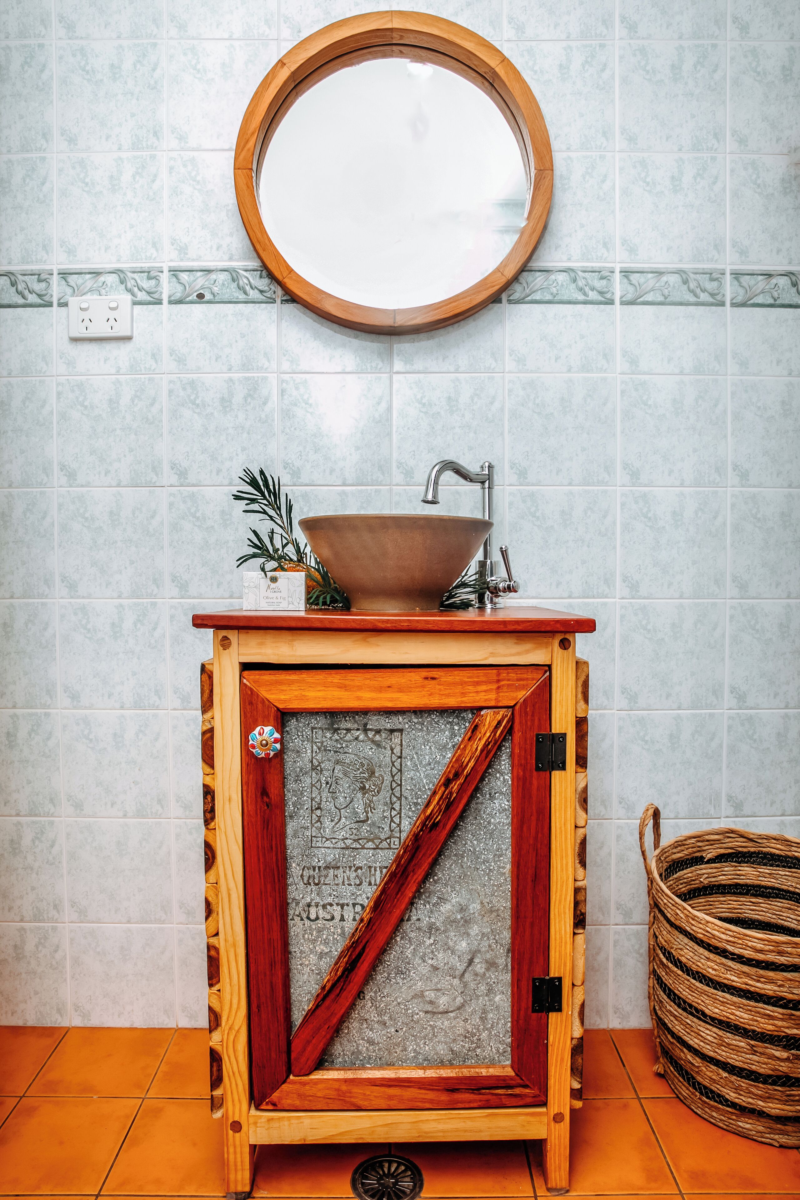 A bathroom with a wooden vanity, a round mirror, and a bowl sink.