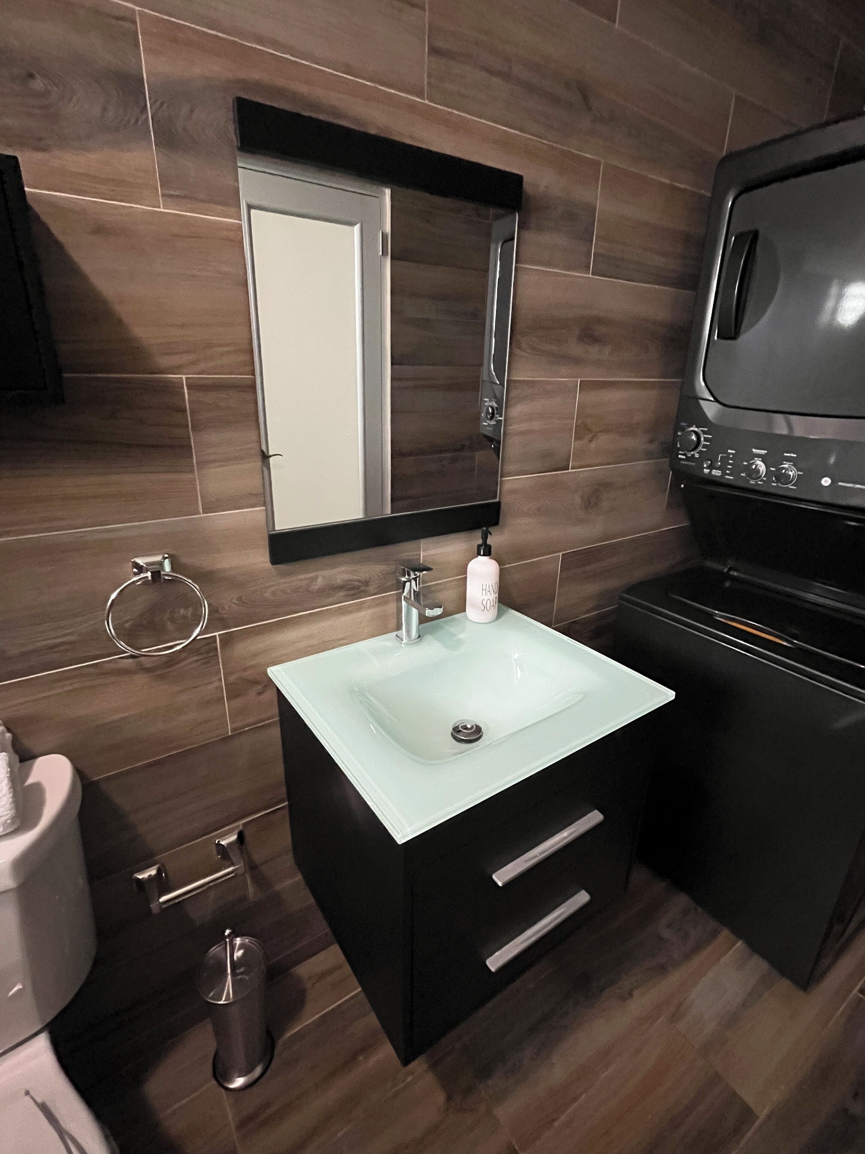 A bathroom with a glass sink, black cabinet, and a mirror above the sink.