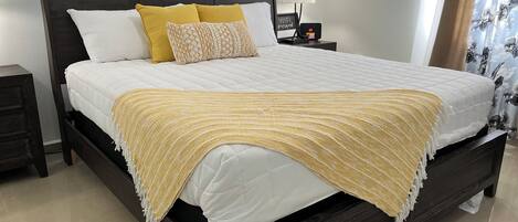 A neatly made bed with a dark headboard, white bedding, and a yellow throw blanket.