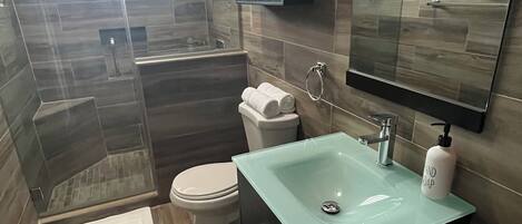 Un baño moderno con un lavabo de vidrio, un inodoro y una zona de ducha.